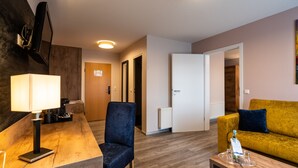 A modern living room with a wooden coffee table, a blue armchair, a yellow sofa, and a white door leading to another room. - AKZENT Hotel Frankenberg (Frankenberg)