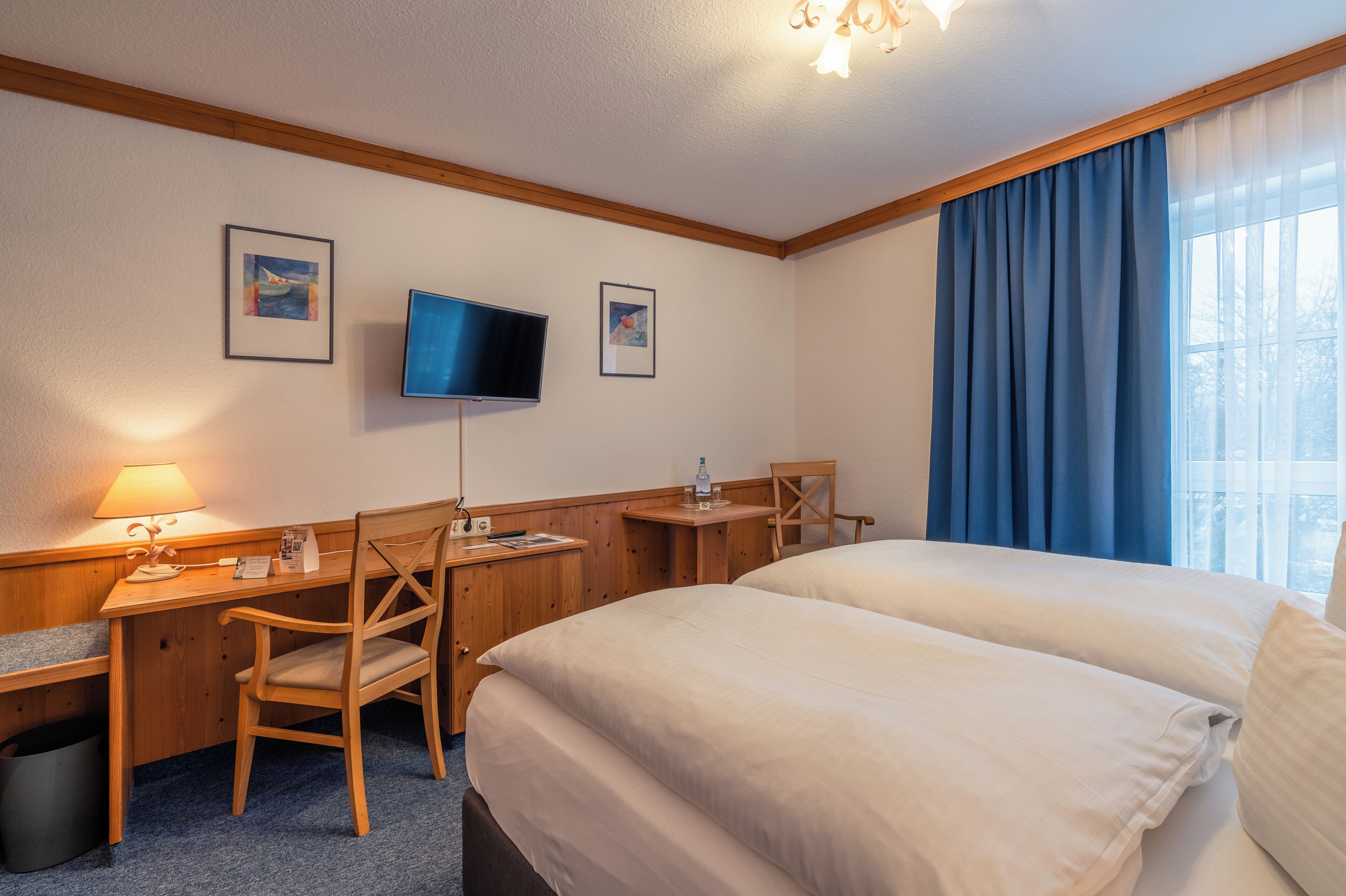 Habitación de hotel con cama, escritorio, silla, televisor y cortinas.