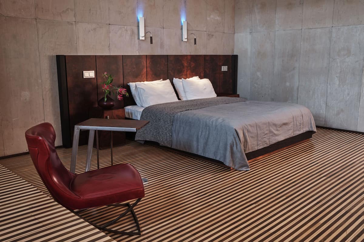 A modern bedroom with a large bed, a red chair, a small table, and a vase of flowers.