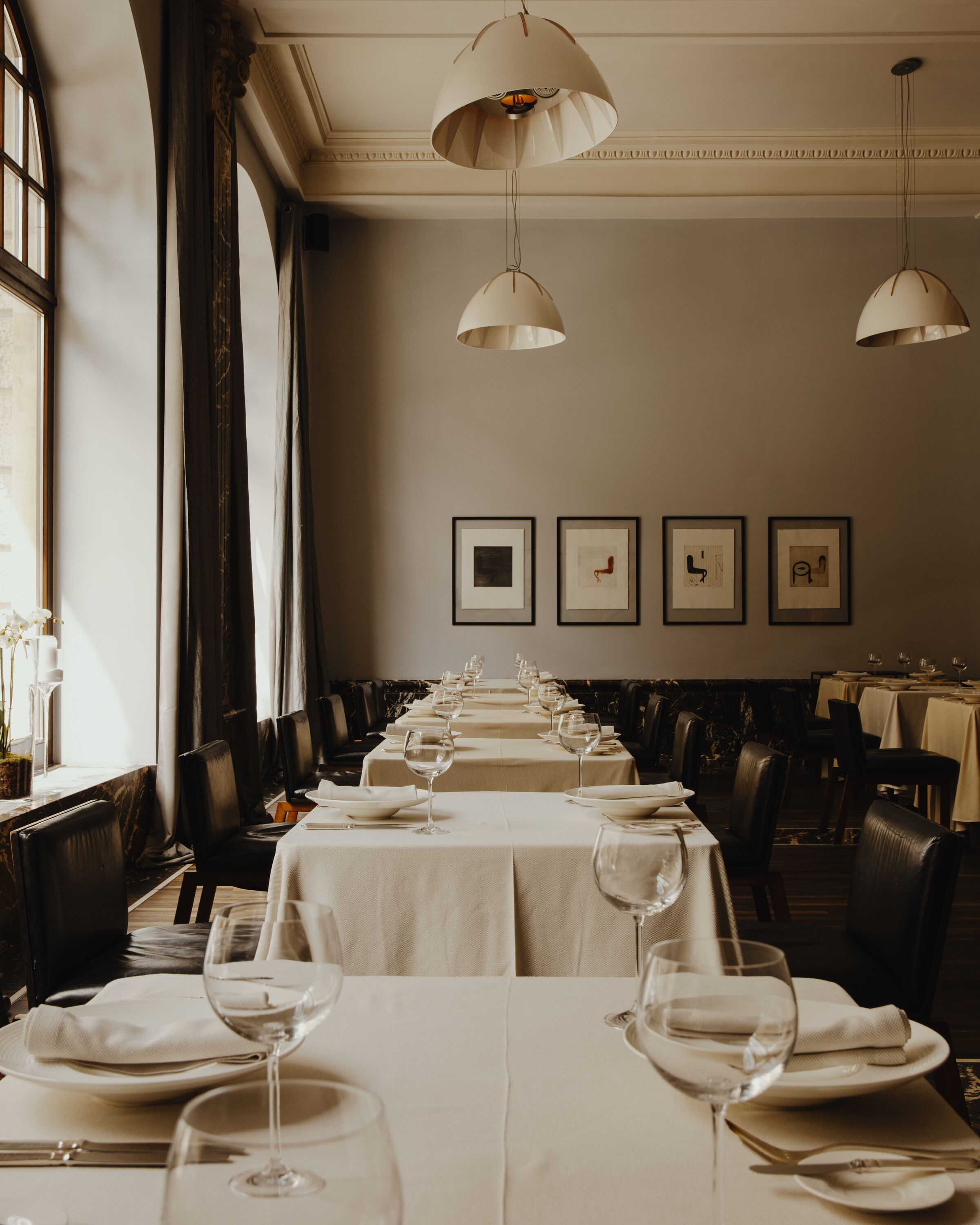 A long dining table set with white tablecloths, wine glasses, and plates, with framed artwork on the wall.