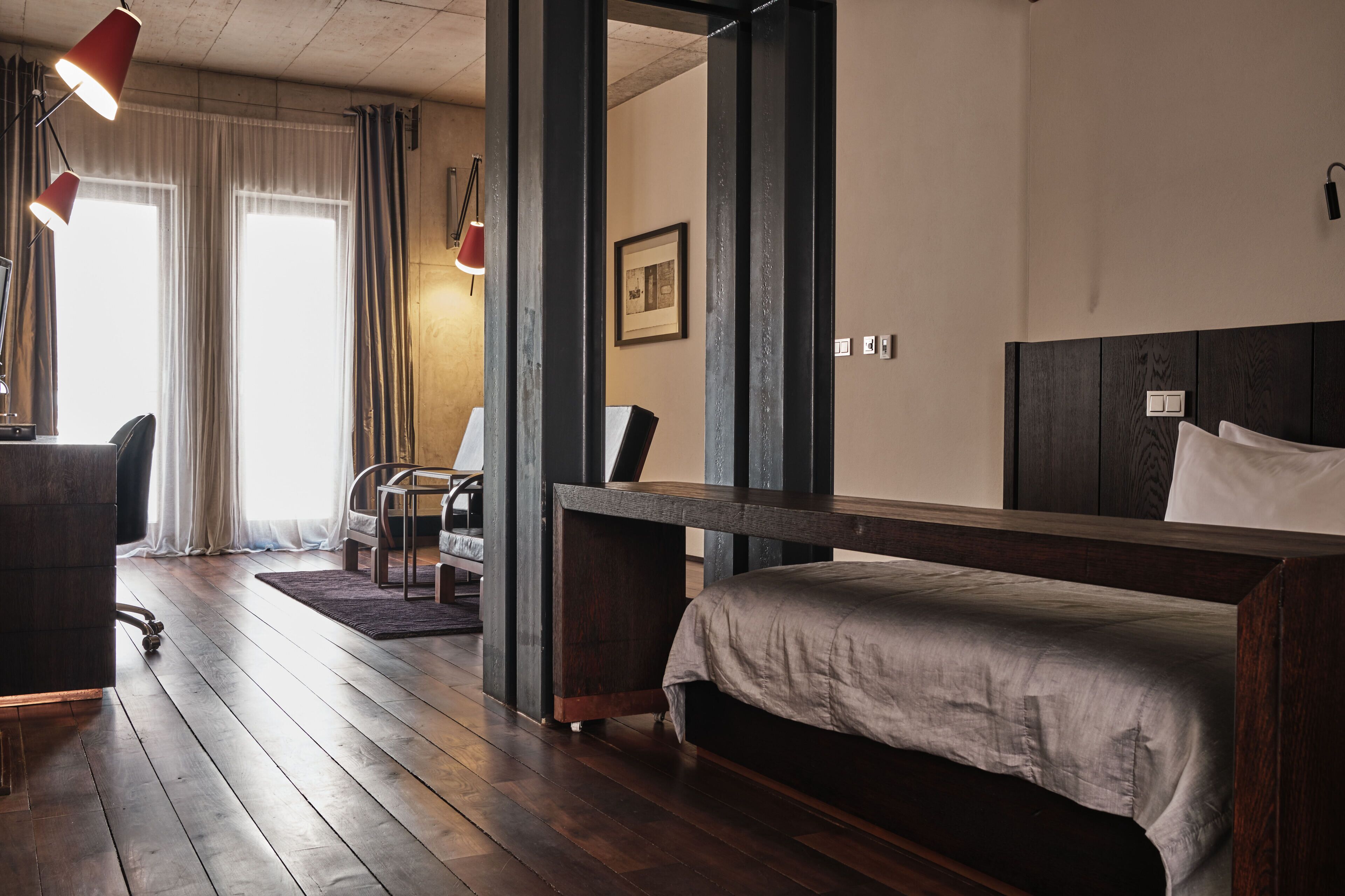 A room with a bed, a desk, a chair, and a large window with curtains.