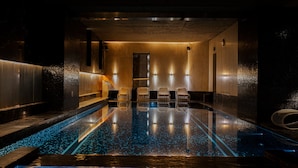 Un área de piscina interior moderna con suelo de cristal, asientos a lo largo de los bordes e iluminación ambiental.