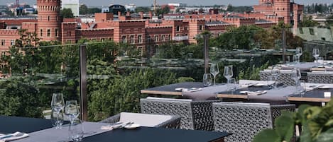 An outdoor dining area with tables set for two, overlooking a cityscape with historic buildings.