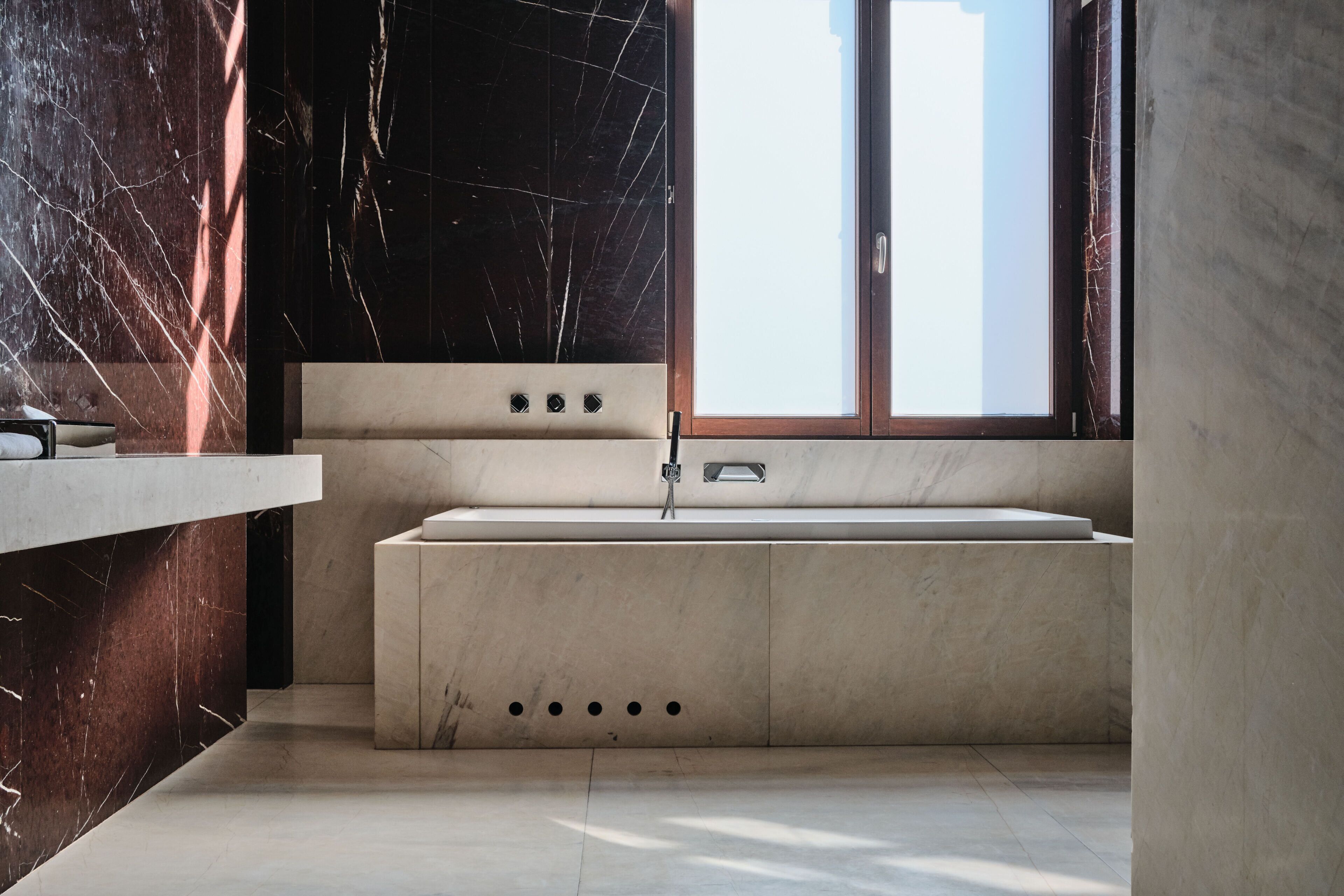 A modern bathroom with a marble vanity, a large bathtub, and a window providing natural light.