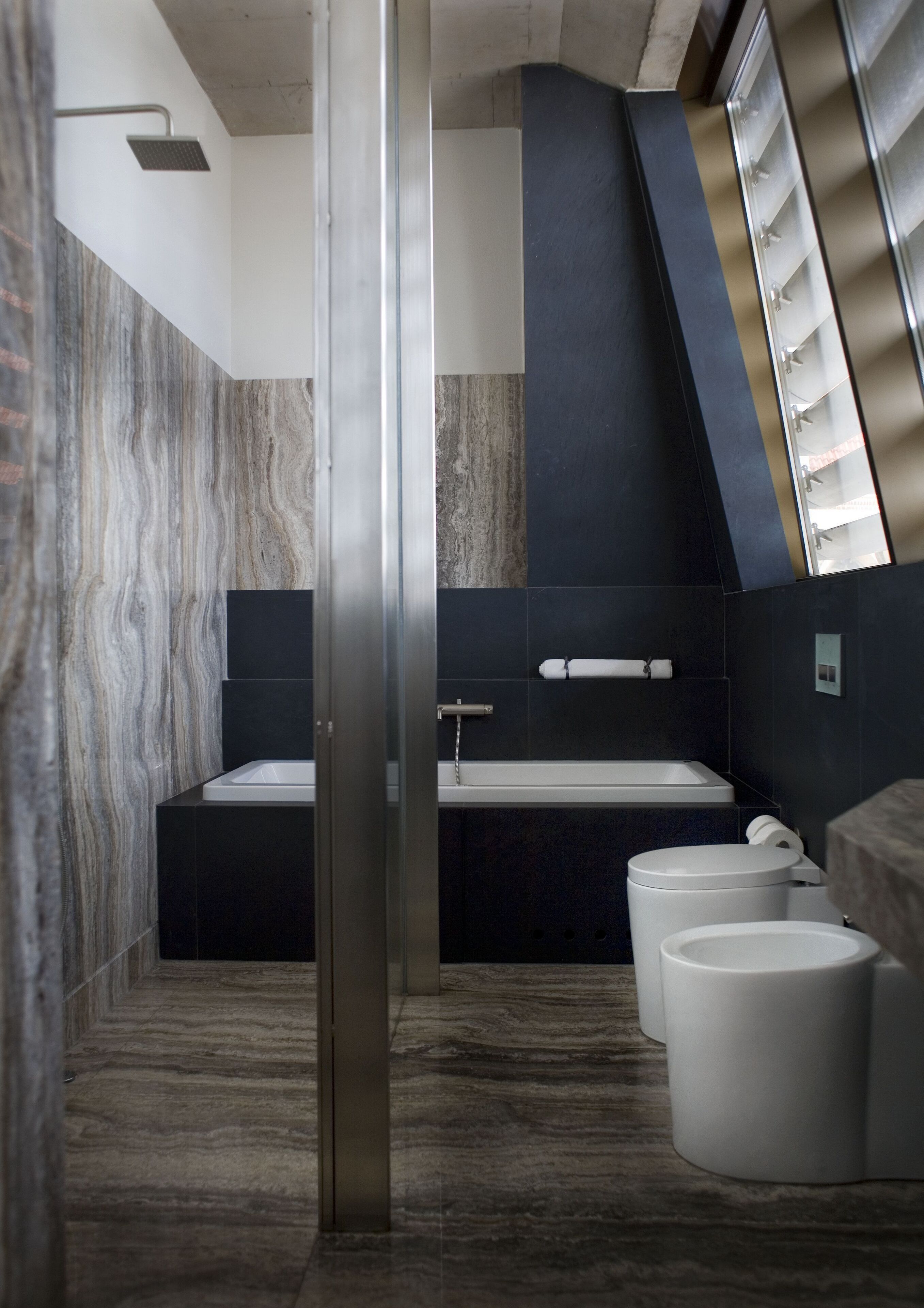 Un baño moderno con pared de mármol, cabina de ducha de cristal y un ventanal grande.