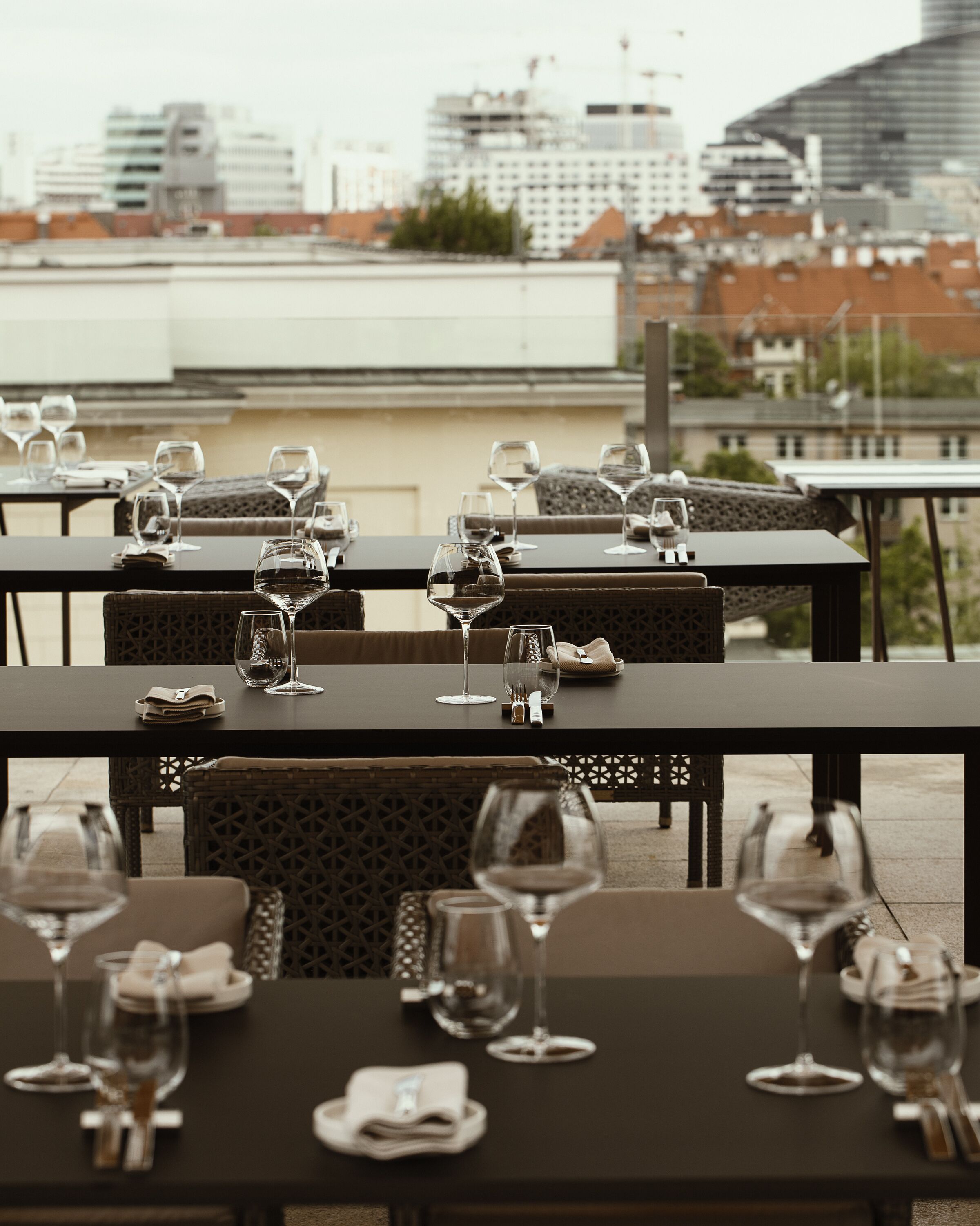 A rooftop dining area with tables set for a meal, featuring wine glasses and cutlery.
