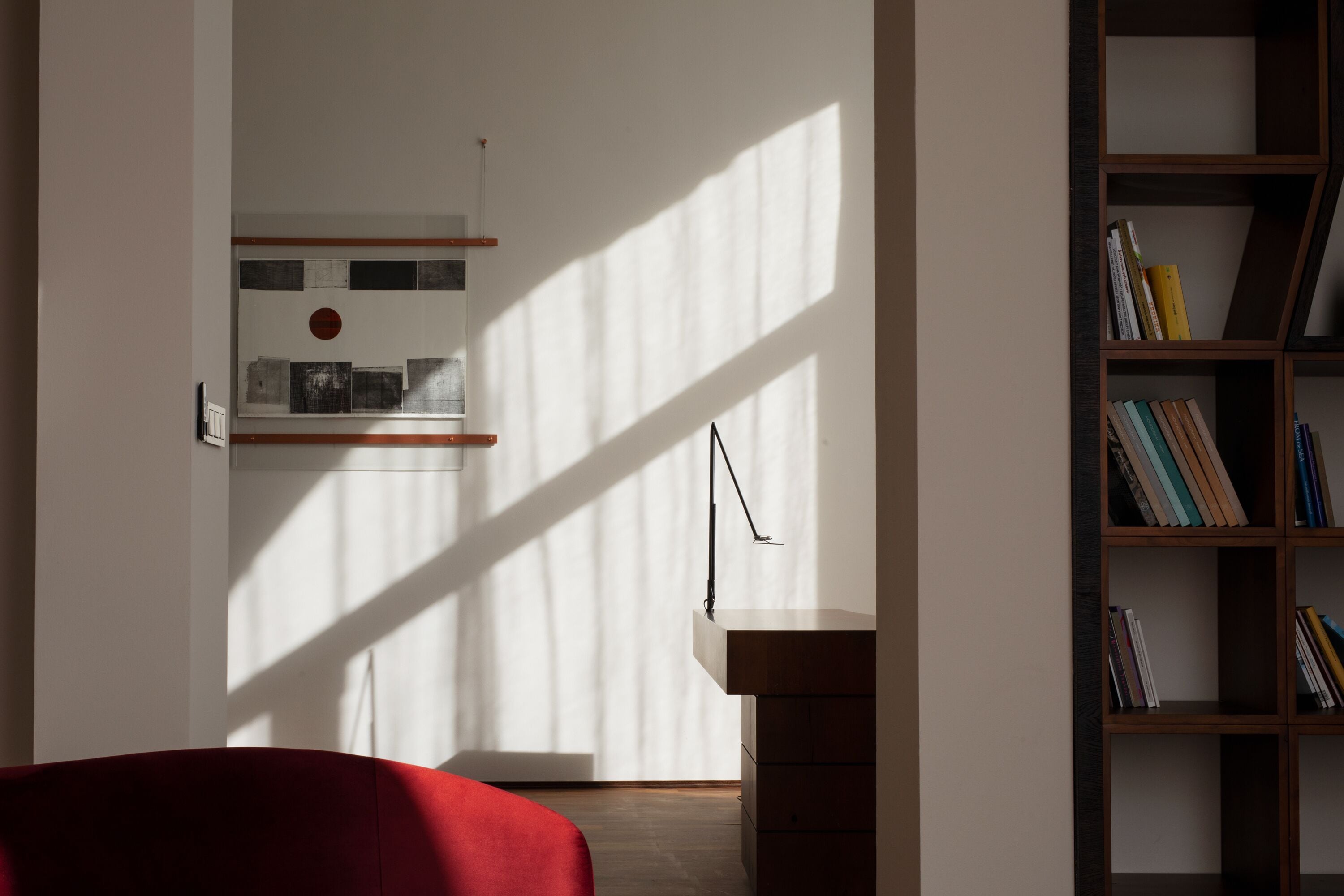 A modern room with a red sofa, a wooden bookshelf, and a wall-mounted shelf with books and decorative items.