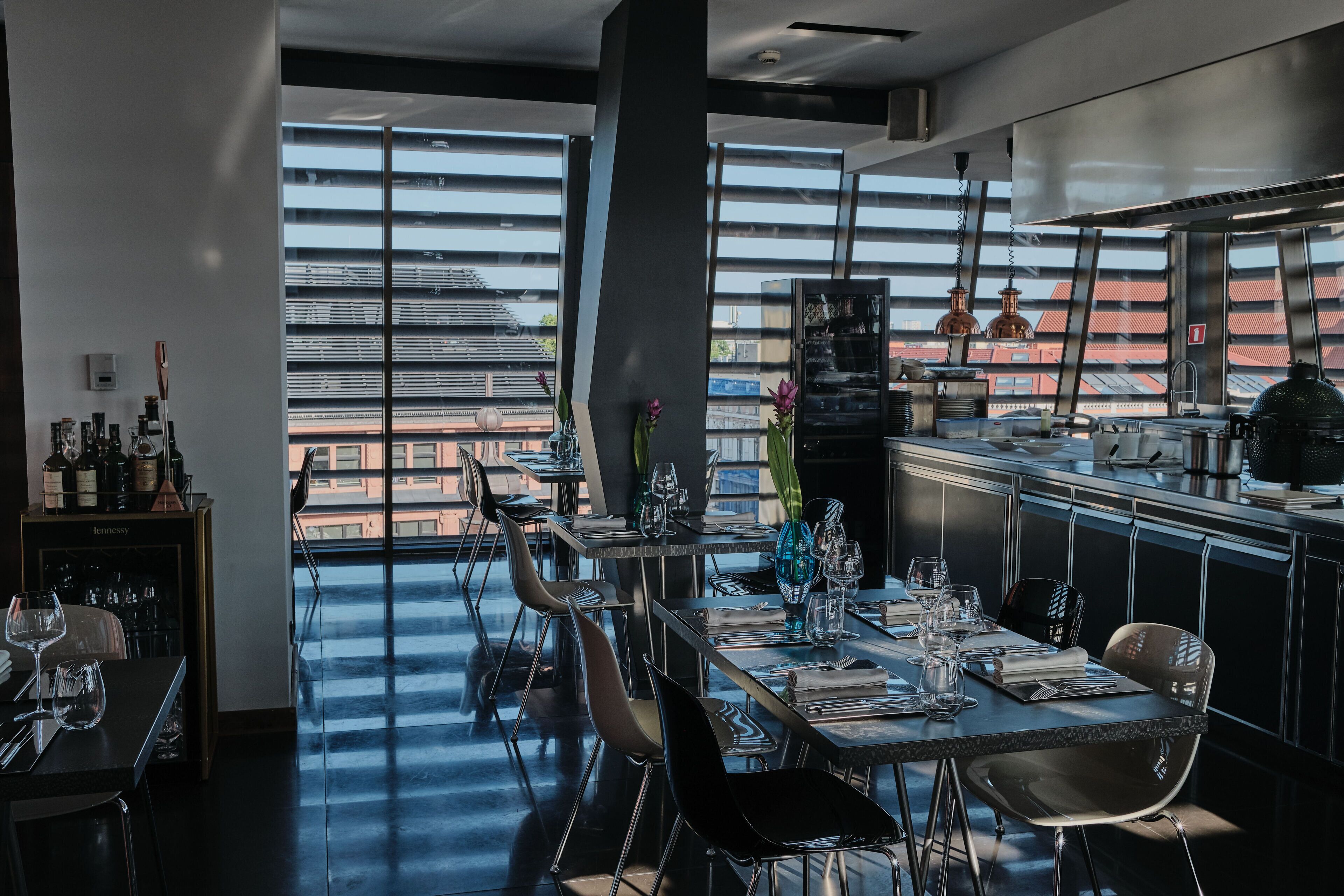Ein modernes Restaurant mit hoher Decke, großen Fenstern und Blick auf die Stadtlandschaft.