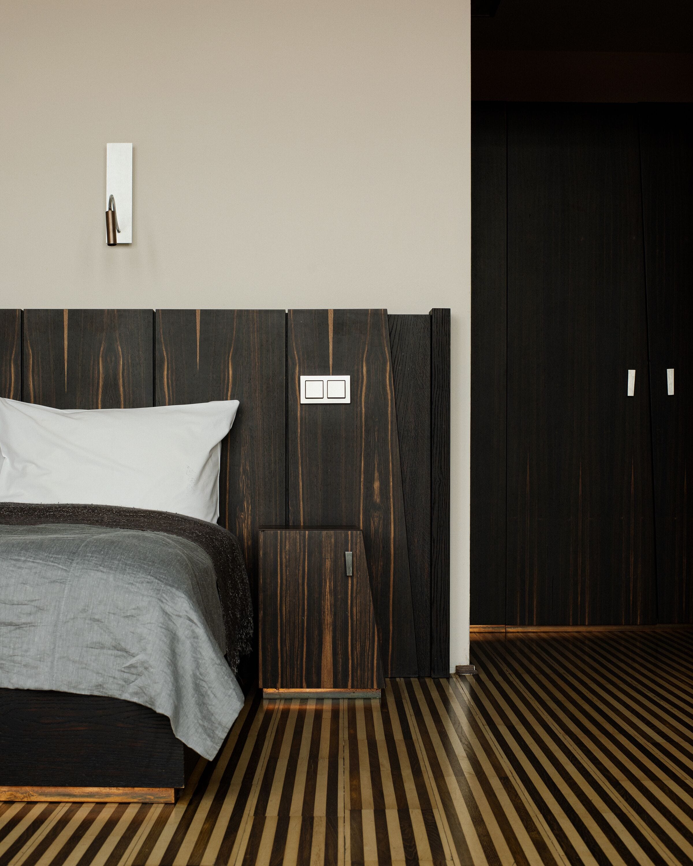 A modern bedroom with a large bed, a wooden headboard, a nightstand, and a wardrobe.