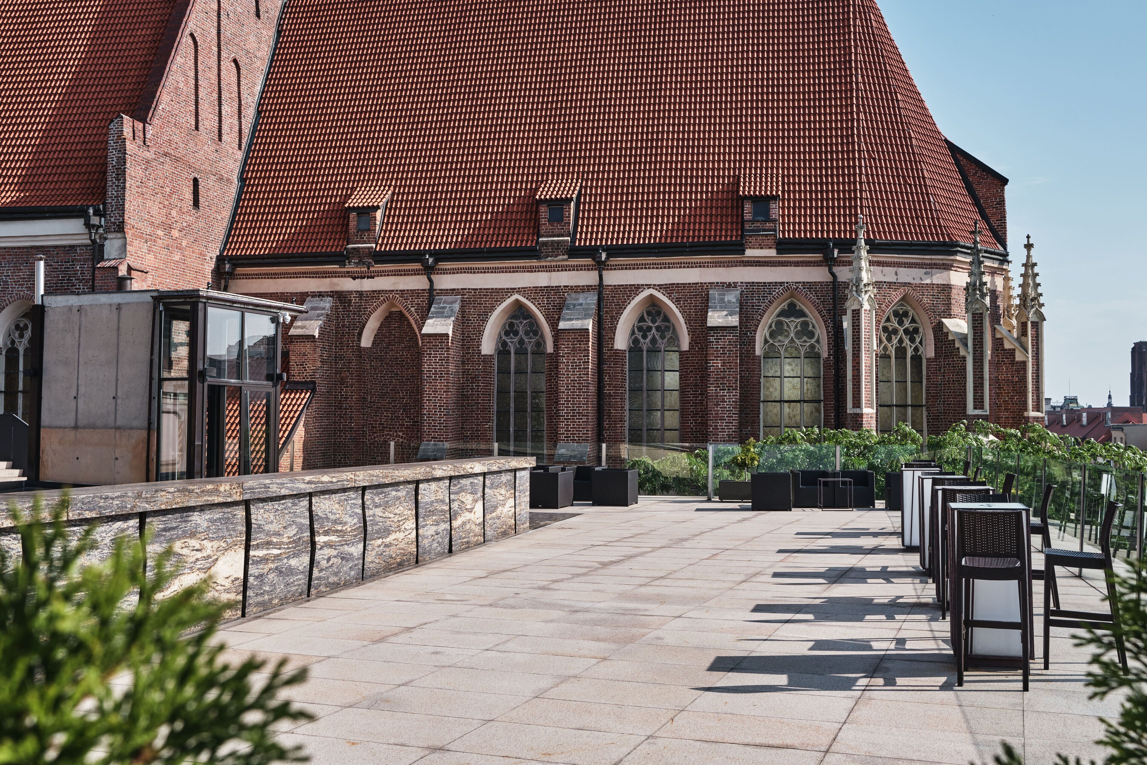 A courtyard with outdoor seating and a brick building with arched windows and a tiled roof.
