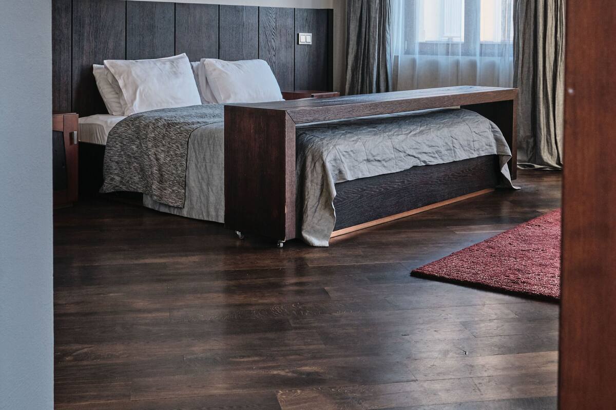 A modern bedroom with a wooden bed, a bench, and a large window with curtains.
