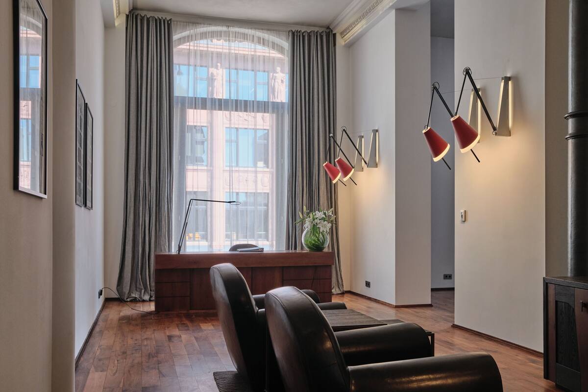 A modern living room with a large window, leather chairs, a small table, and wall-mounted lighting.