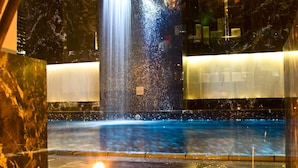 Un área de piscina con cascada, paredes de mármol y una vela encendida.