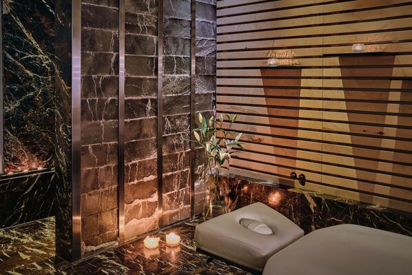 Un espace de détente avec un mur en pierre, des lambris en bois, une table de massage et des bougies.