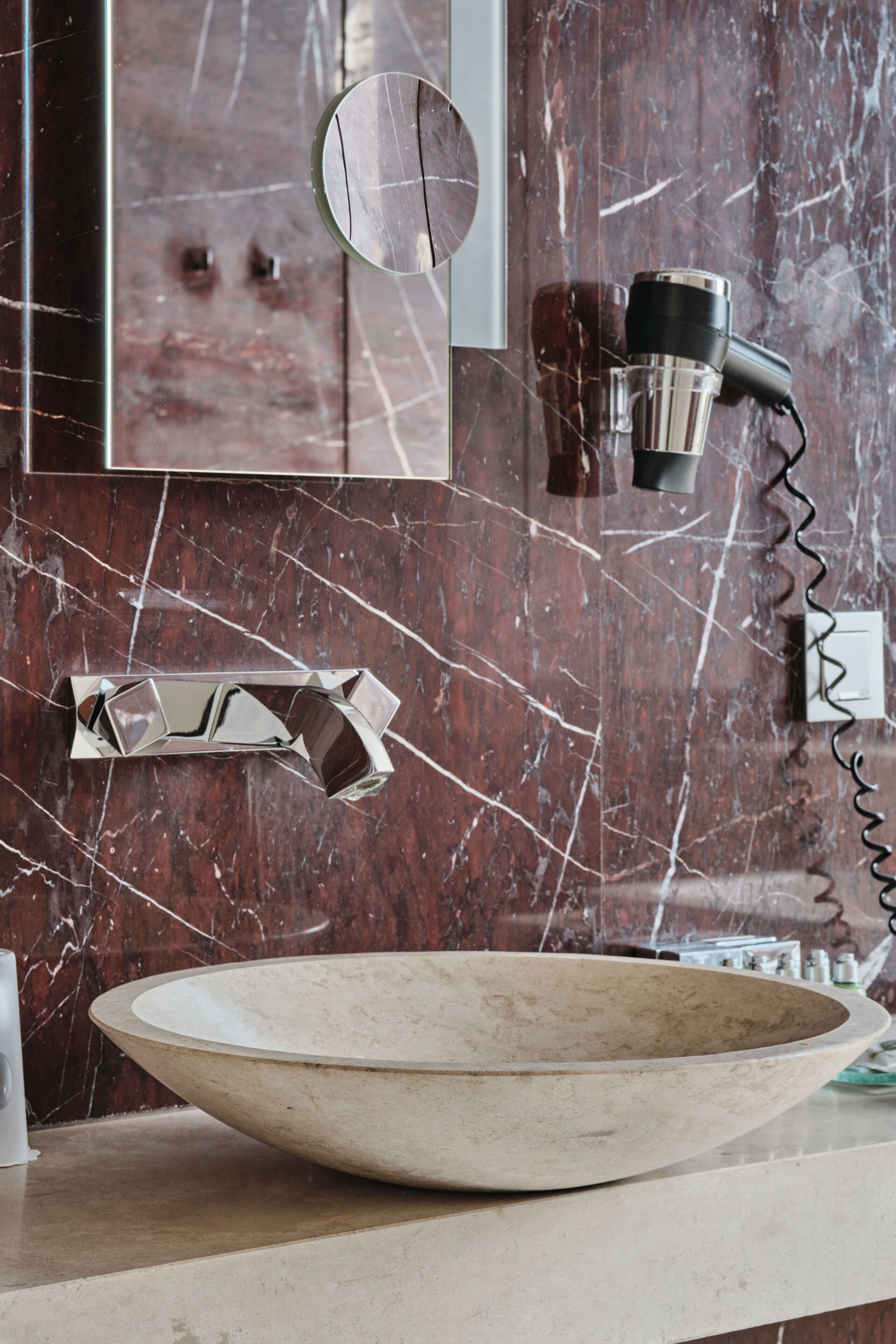A bathroom with a marble sink, a modern faucet, a hairdryer, and a mirror.