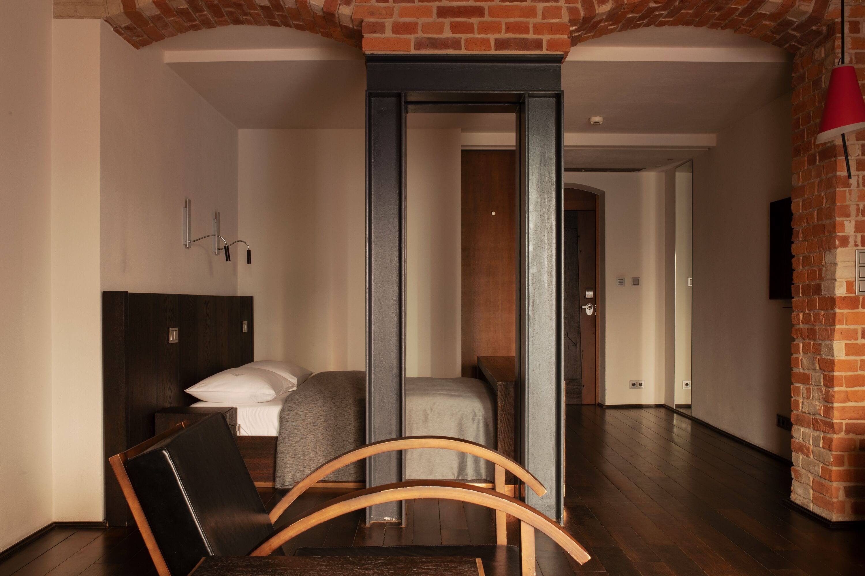 Una camera d'albergo moderna con un letto, una sedia di legno, una scrivania e un muro in mattoni.