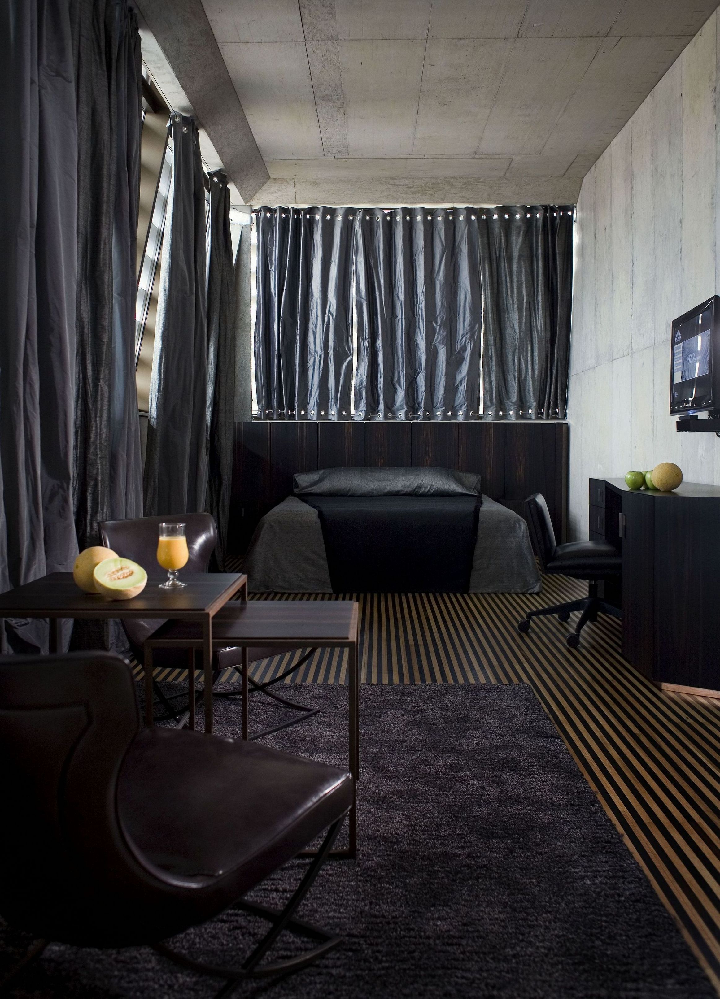 Une chambre d’hôtel moderne équipée d’un lit, d’un bureau, d’une chaise, d’une télévision et d’une fenêtre avec des rideaux.