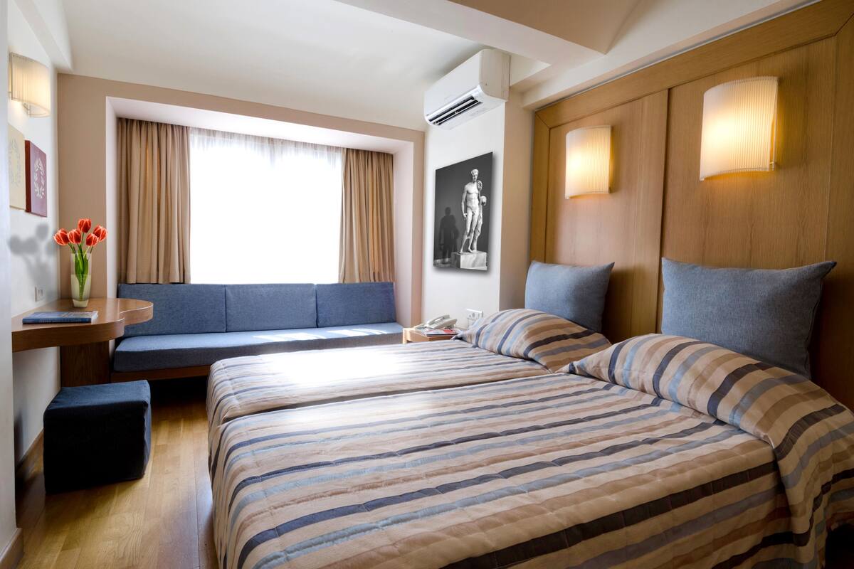 Une chambre d’hôtel avec deux lits, un canapé, un bureau et une fenêtre avec des rideaux.