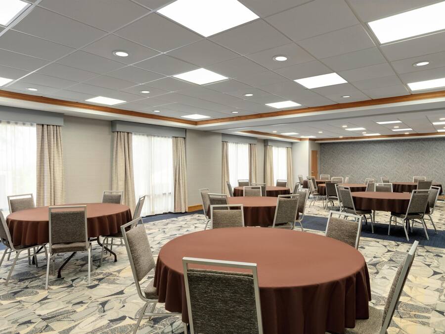 A conference room with multiple round tables and chairs, large windows with curtains, and a patterned carpet.