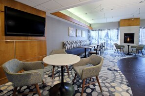 Un moderno vestíbulo de hotel con un televisor de pantalla plana, una chimenea, una zona de estar con sofás y sillones, y una alfombra estampada.