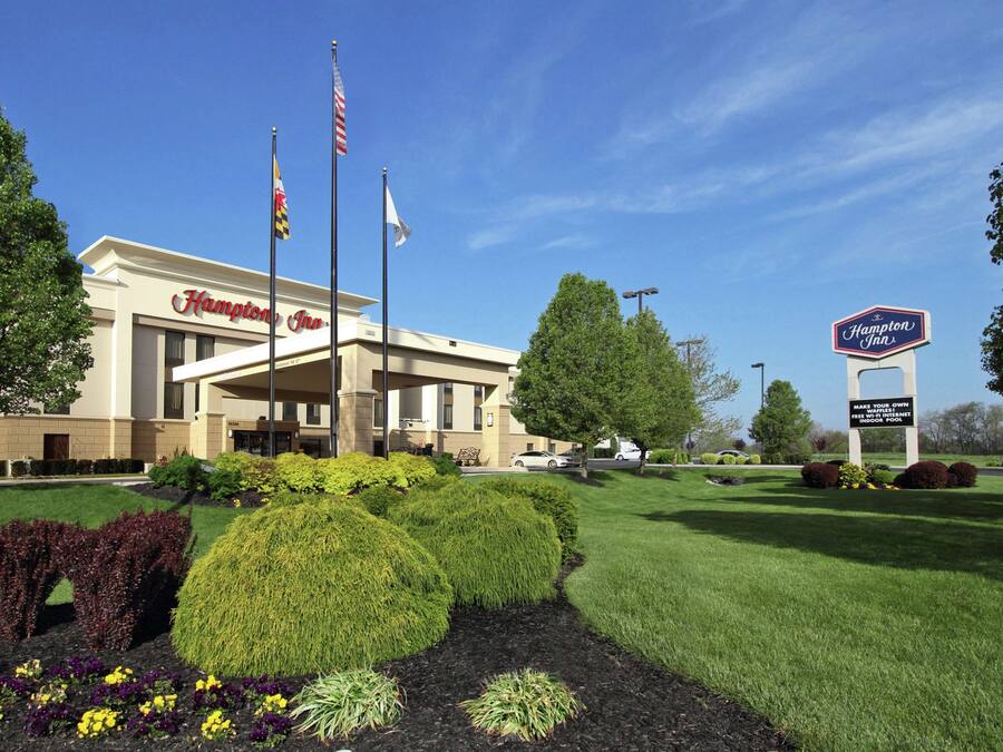 A Hampton Inn hotel with a well-maintained lawn, American flags, and a sign indicating free parking and a pool.
