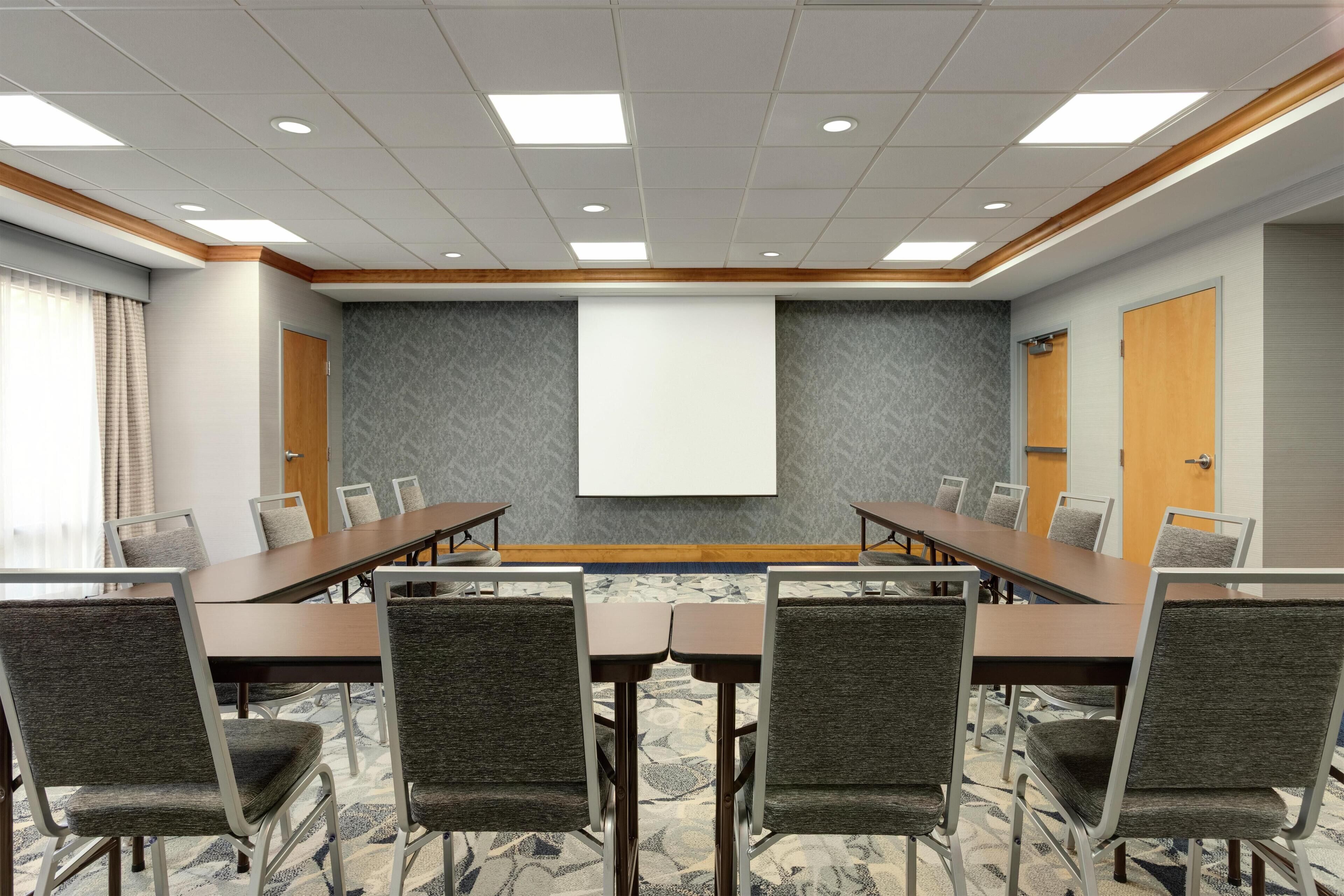 A conference room with a long table, chairs, a projector screen, and a carpeted floor.