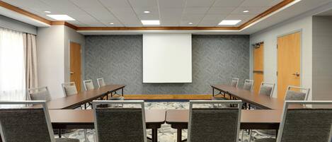 A conference room with a long table, chairs, a projector screen, and a carpeted floor.