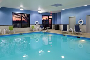 Una piscina interior con agua cristalina, rodeada de sillones de descanso y vistas al atardecer a través de un amplio ventanal.