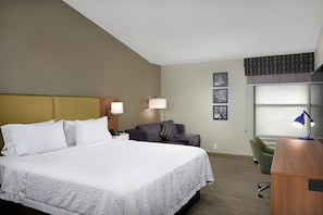 Relax in this inviting room with a large bed, sofa, and desk, offering a comfortable seating area and a window with a view.