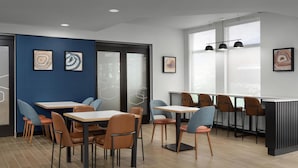 A modern dining area with tables and chairs, framed artwork on the walls, and large windows providing natural light. - Hampton Inn Butte (Butte)