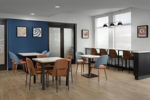 Un comedor moderno con mesas y sillas, obras de arte en las paredes y amplios ventanales que permiten la entrada de luz natural.