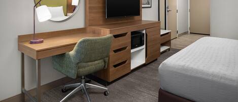 Habitación de hotel con un escritorio de madera, televisión, espejo, cama y puerta.