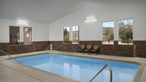 An indoor swimming pool with clear views through large windows, a tiled floor, and a seating area with chairs.