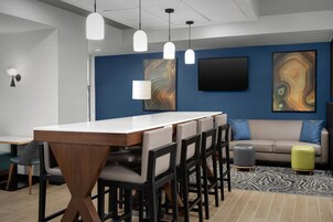 Un interior moderno con una larga mesa de comedor, varias sillas, un sofá y un televisor de pantalla plana montado en la pared.