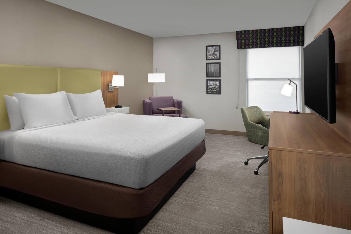 A hotel room with a large bed, a desk, a chair, and a television.