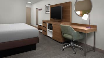 Une chambre d’hôtel avec un lit, un bureau avec un ordinateur, une télévision, un miroir et une lampe.