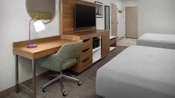 Habitación de hotel con un escritorio de madera, una silla de oficina verde, un televisor de pantalla plana, una cama y una puerta.