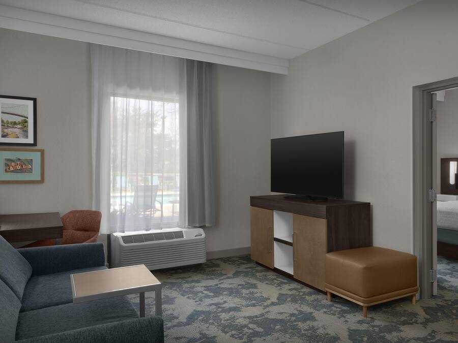 Una habitación de hotel con sofá, televisor en un mueble, ventana con cortinas y cama.