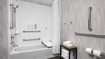 A modern bathroom with a bathtub, shower, and handrails.