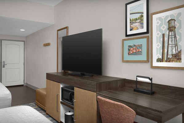 Une chambre d’hôtel moderne équipée d’une télévision à écran plat, d’un bureau en bois, d’un four à micro-ondes et d’une chaise.