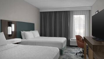 A hotel room with two beds, a desk, a TV, and a large window with curtains.
