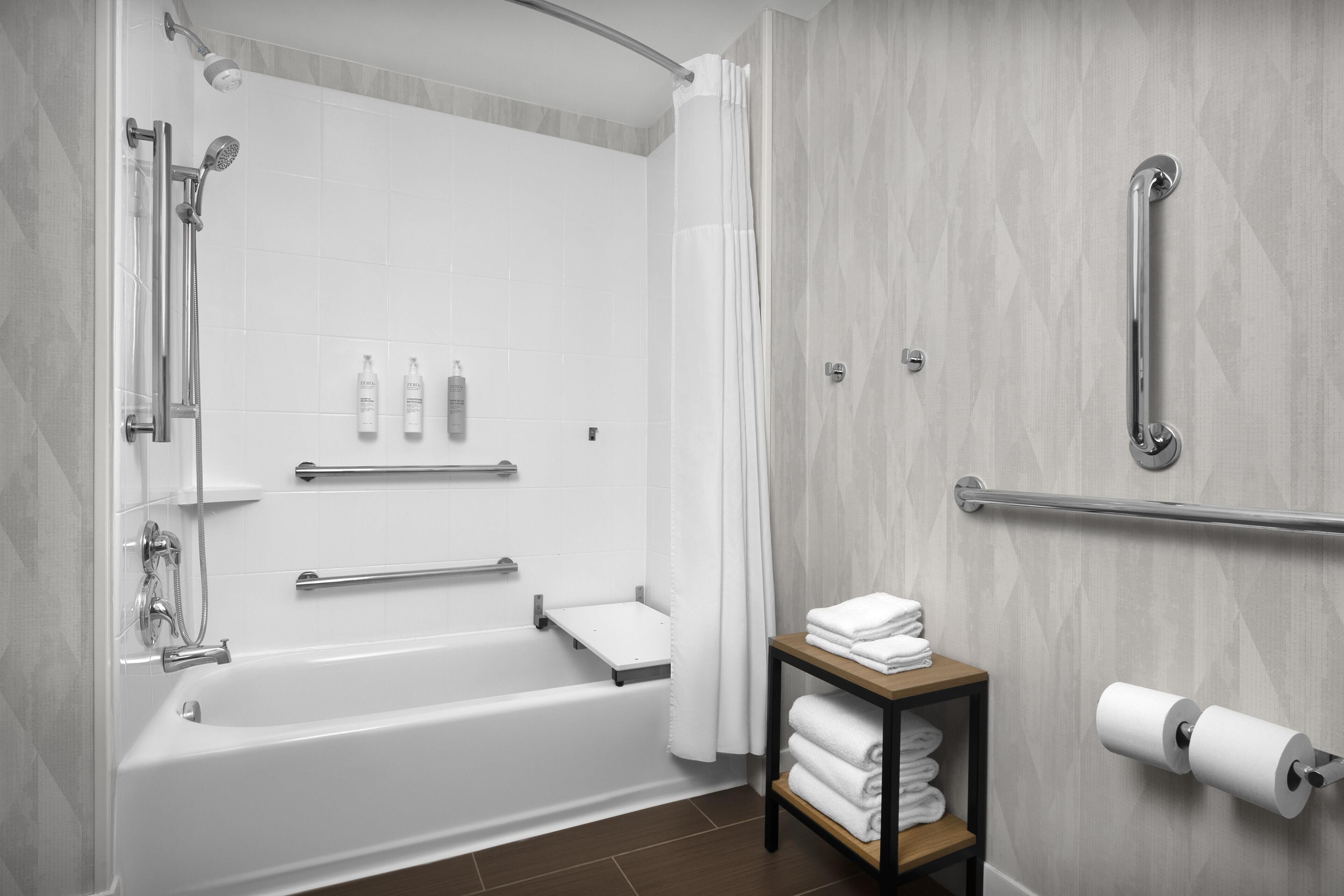 A modern bathroom with a bathtub, shower, grab bars, a towel rack, and a toilet paper holder.