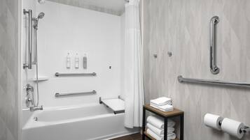 A modern bathroom with a bathtub, shower, grab bars, a towel rack, and a toilet paper holder.
