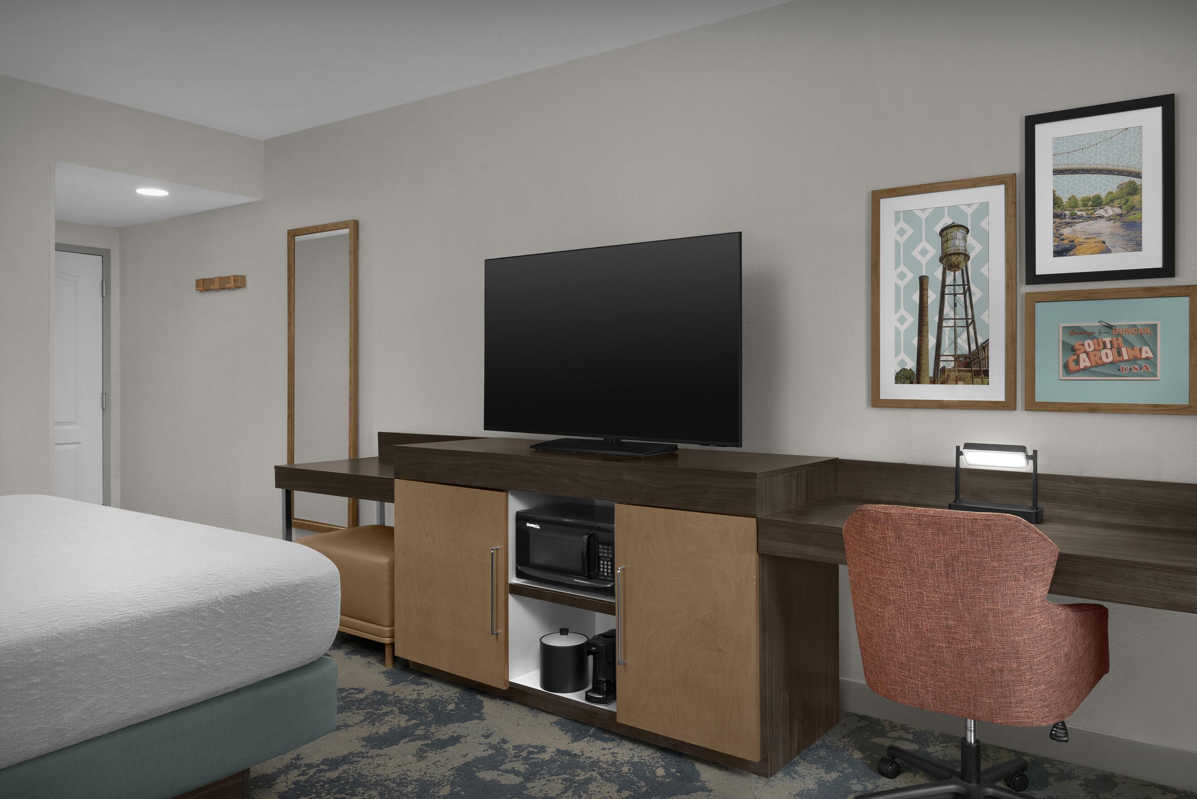 A hotel room with a bed, a desk with a television, a chair, and a microwave.