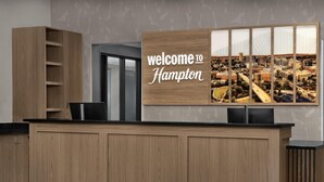 A reception desk with a 'Welcome to Hampton' sign and a cityscape photograph. - Hampton Inn & Suites Greenville/Spartanburg I-85, SC (Duncan)