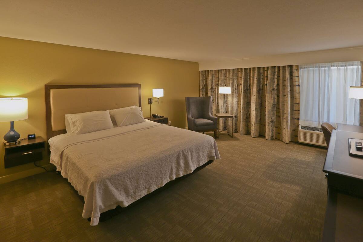 A hotel room with a large bed, a desk, a chair, and a lamp.