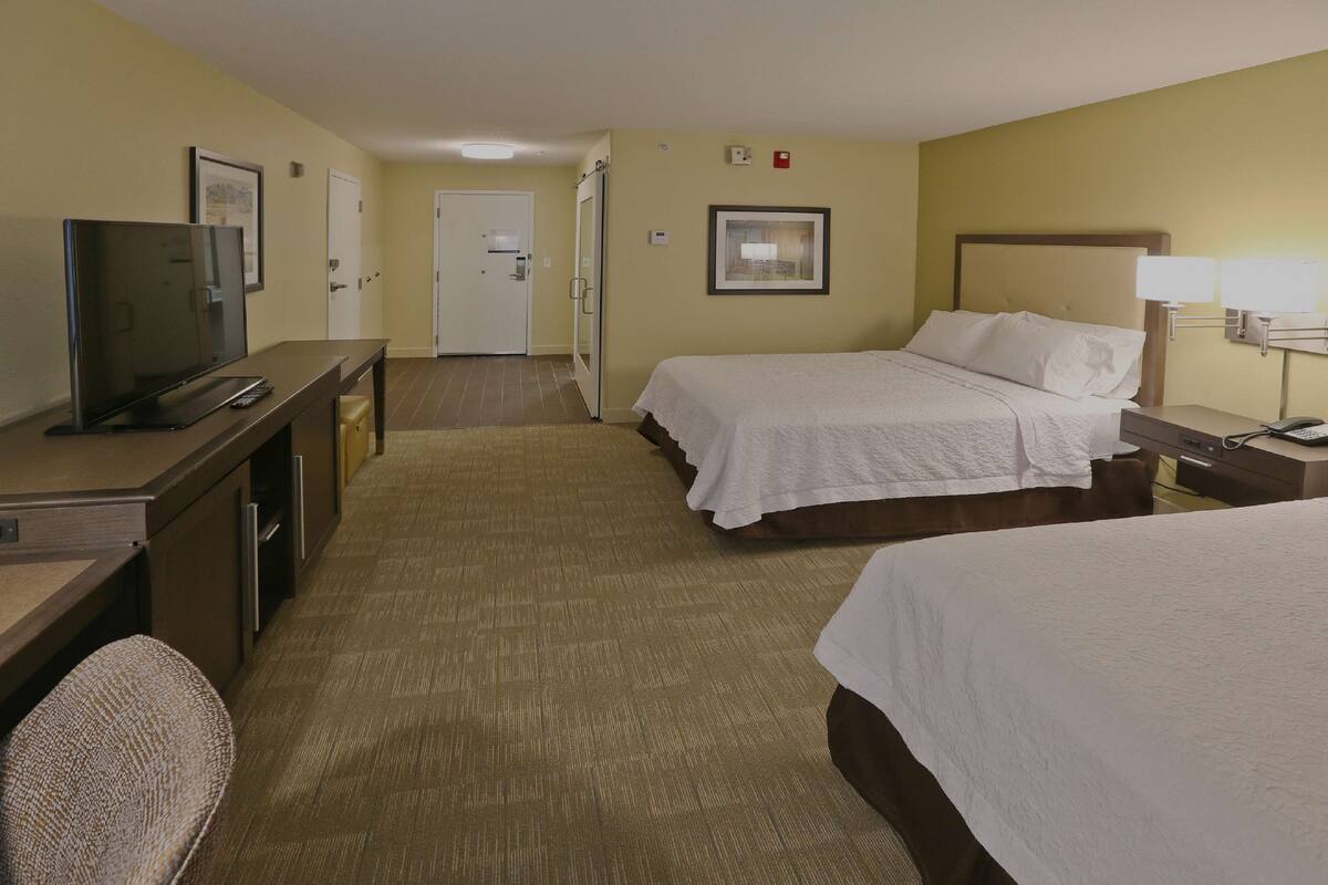 A hotel room with two beds, a desk with a television, and a chair.