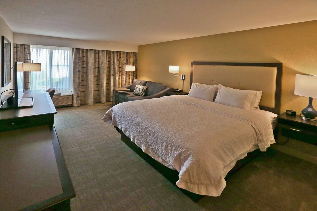 A hotel room with a large bed, a desk, a chair, and a TV.