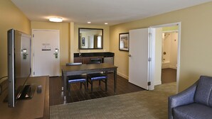 Camera d'albergo con zona pranzo, divano, televisore e bagno visibile attraverso una porta aperta.