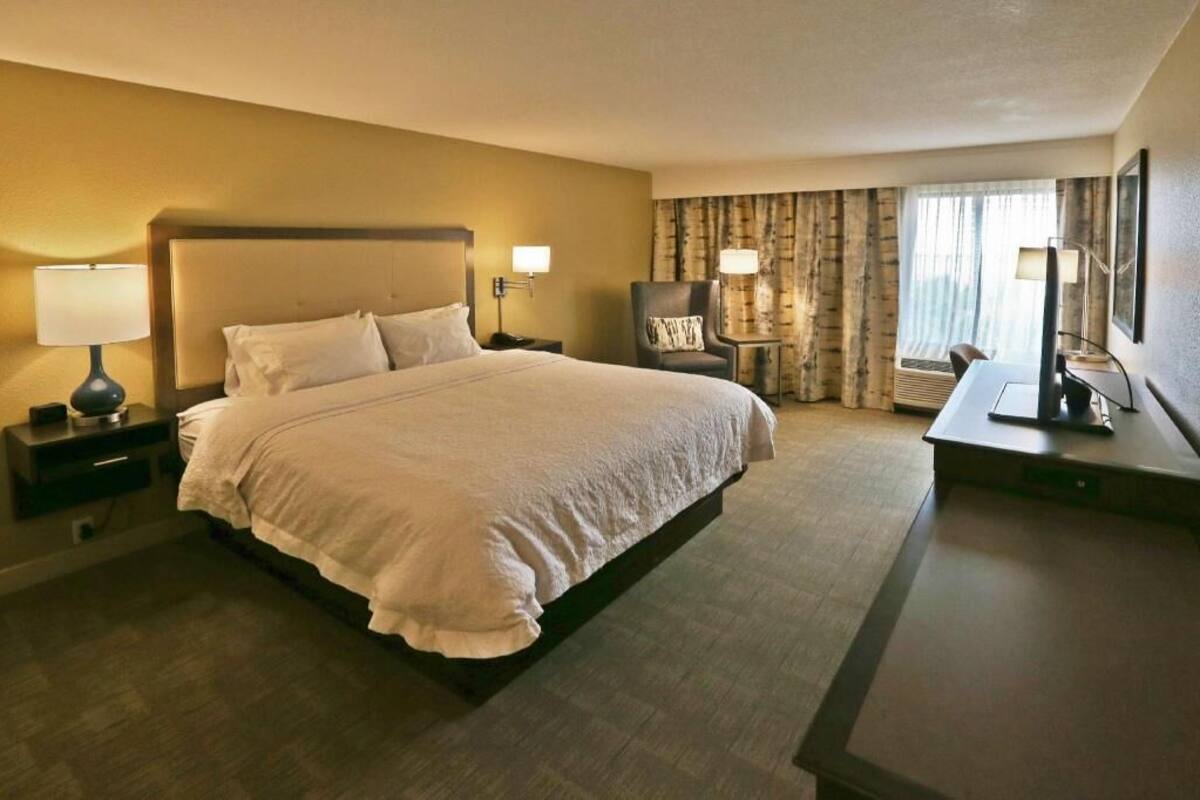 A hotel room with a large bed, a desk, a chair, and a lamp.